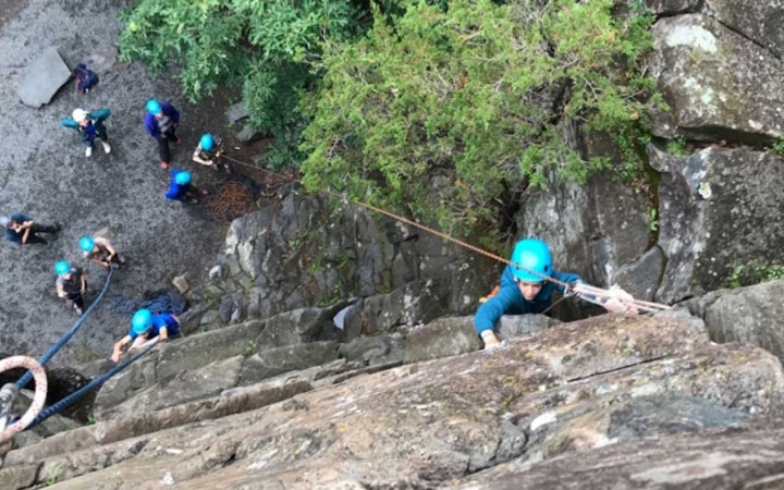 a student scales a rock face as the group looks on 